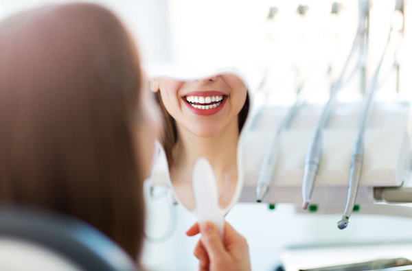 Woman looking at her smile in a mirror after her restorative dental procedure in Upland CA
