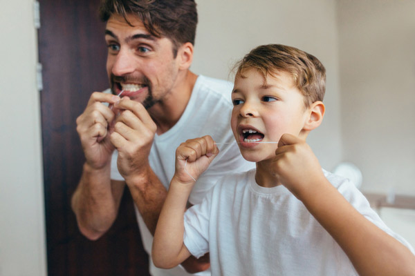 Young boy and father flossing teeth next to each other in bathroom.