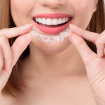 Woman holding clear Invisalign aligners showing proper Invisalign care with confident smile and white teeth