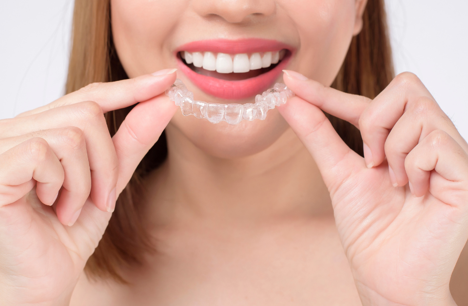 Woman holding clear Invisalign aligners showing proper Invisalign care with confident smile and white teeth