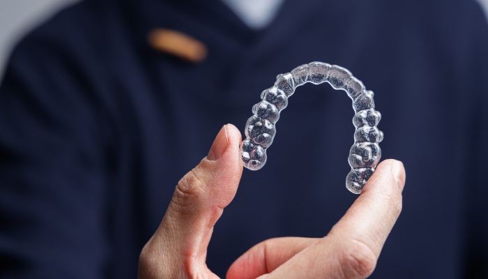 Hands holding clear Invisalign aligner demonstrating proper Invisalign care and handling techniques