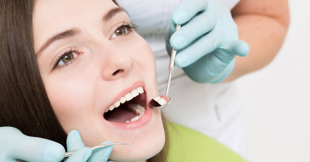 Woman in dental chair with mouth open receiving dental examination from dentist wearing teal gloves