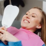 Smiling woman in dental chair looking at mirror examining her teeth