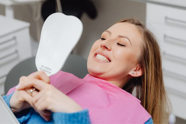 Smiling woman in dental chair looking at mirror examining her teeth