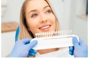 Smiling woman in dental chair with dentist holding tooth shade guide to match teeth color