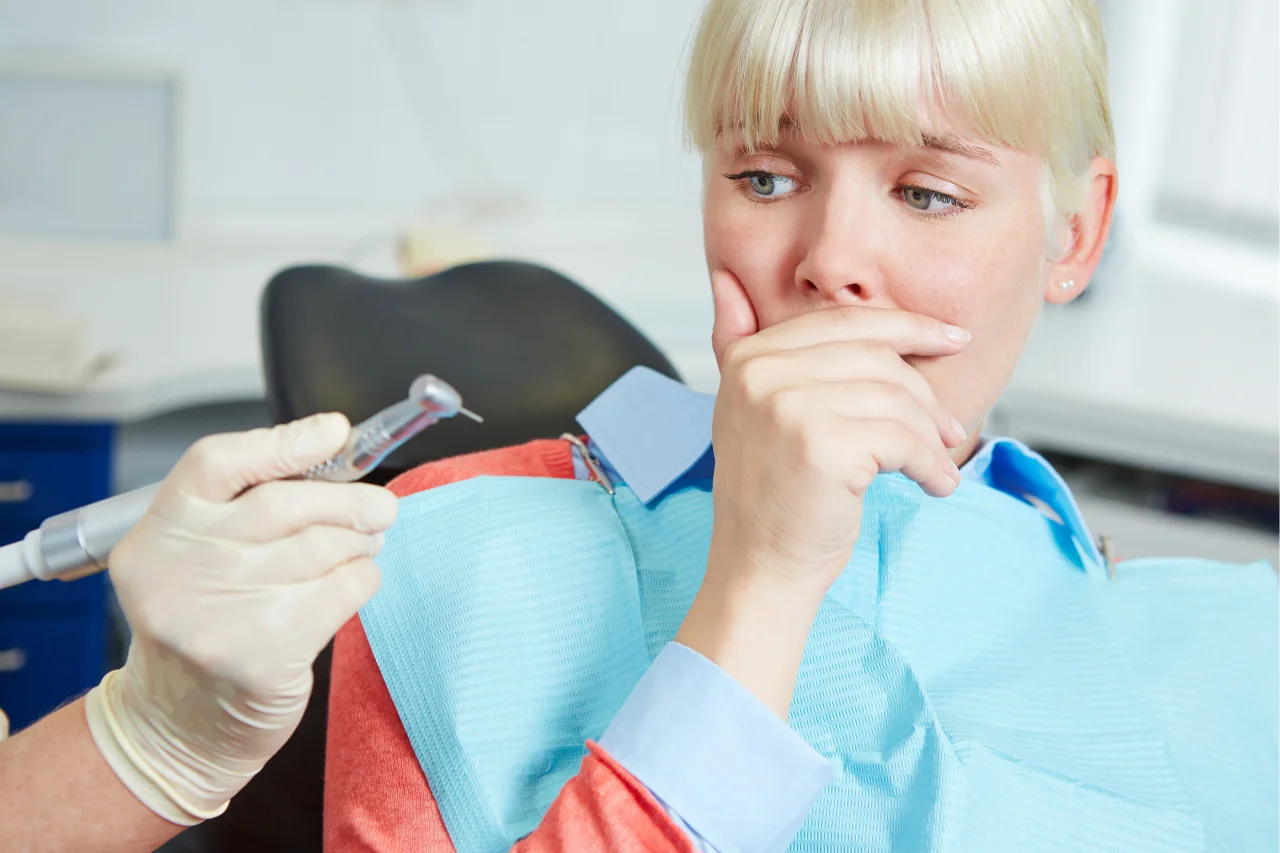 Anxious patient sitting in dental chair looking worried with dentist in background