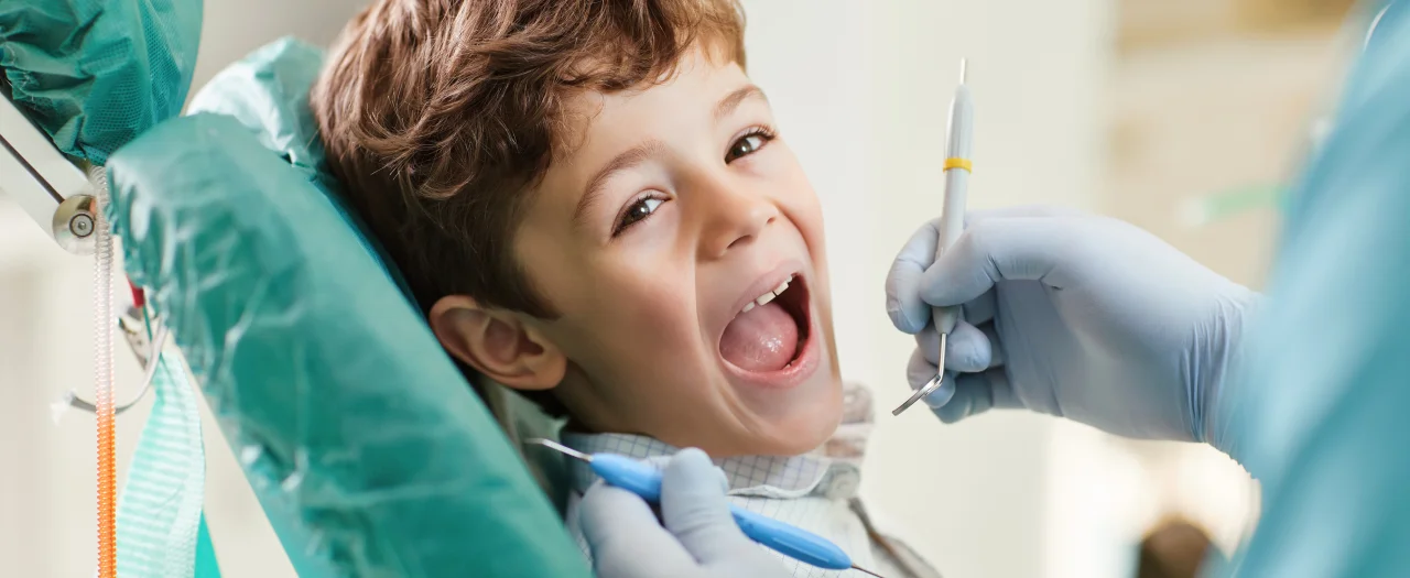 Young boy with mouth open wide in dental chair during dental examination with dentist wearing gloves