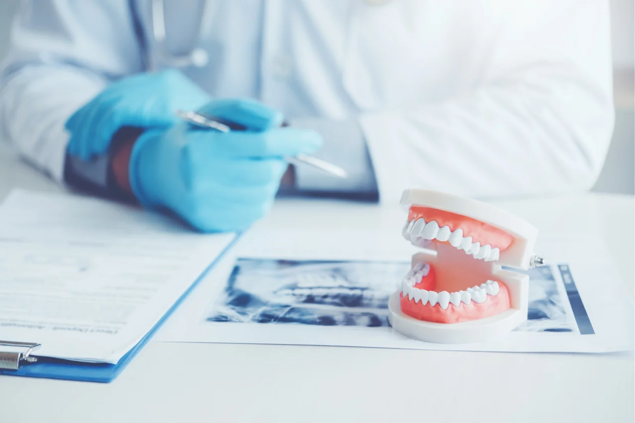 Set of dentures on white surface with dental tools and blue gloves in background