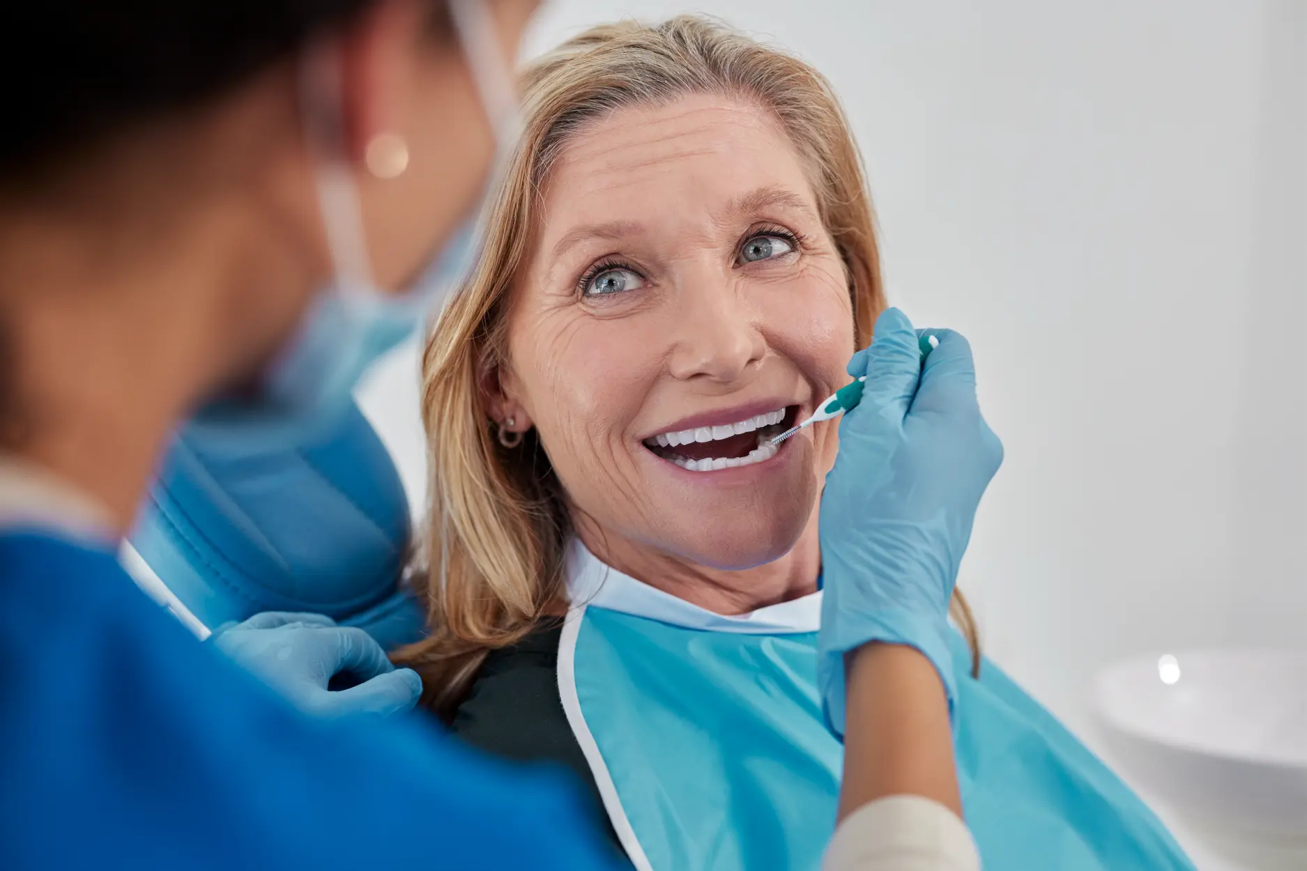 Woman in dental chair smiling during examination with dentist wearing blue gloves