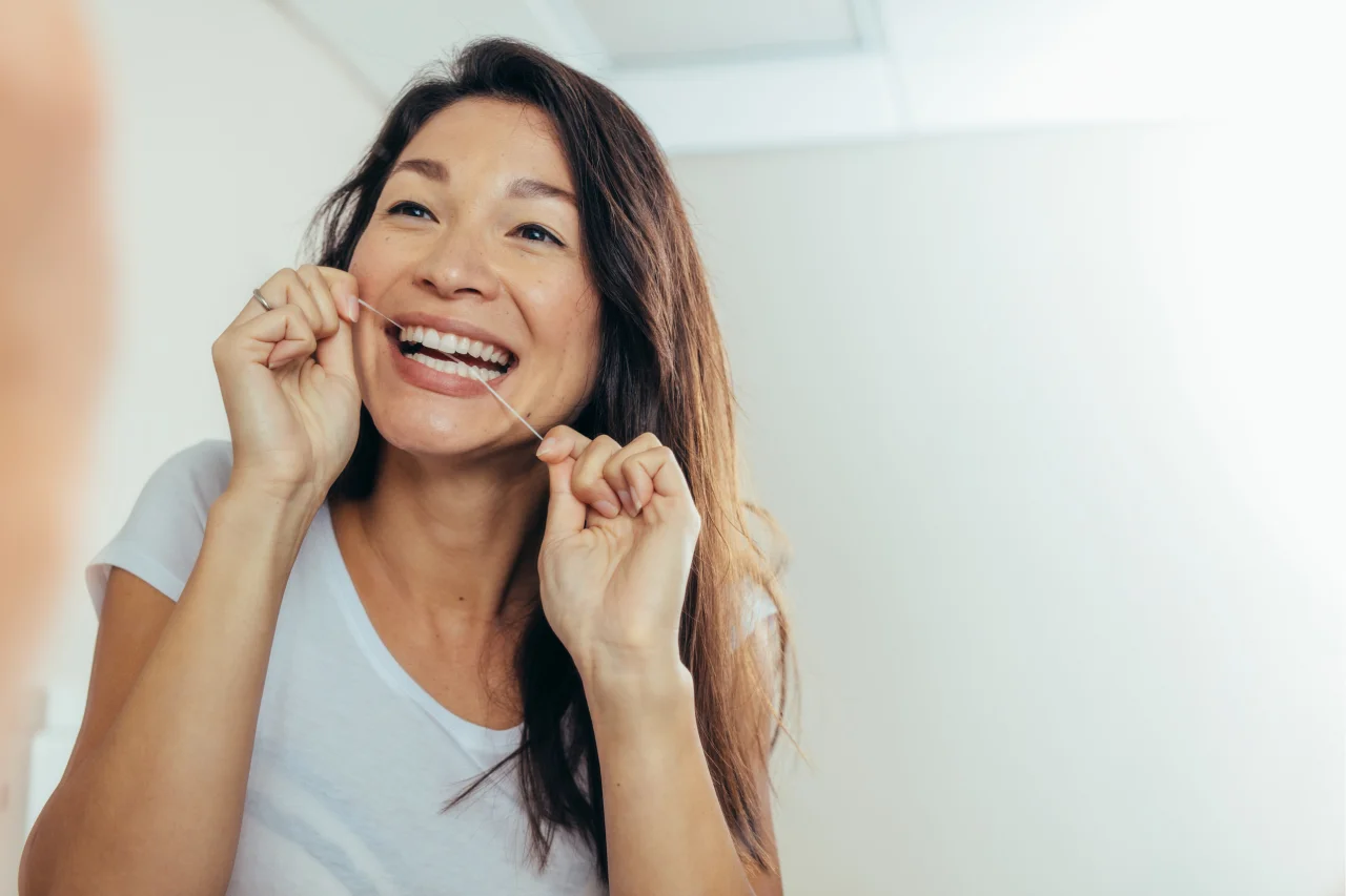 Smiling Asian woman flossing teeth with dental floss demonstrating proper technique