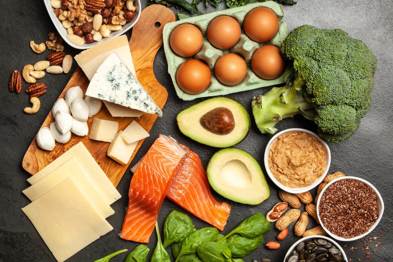 Container with healthy foods including salmon, avocado, broccoli, nuts, eggs and vegetables