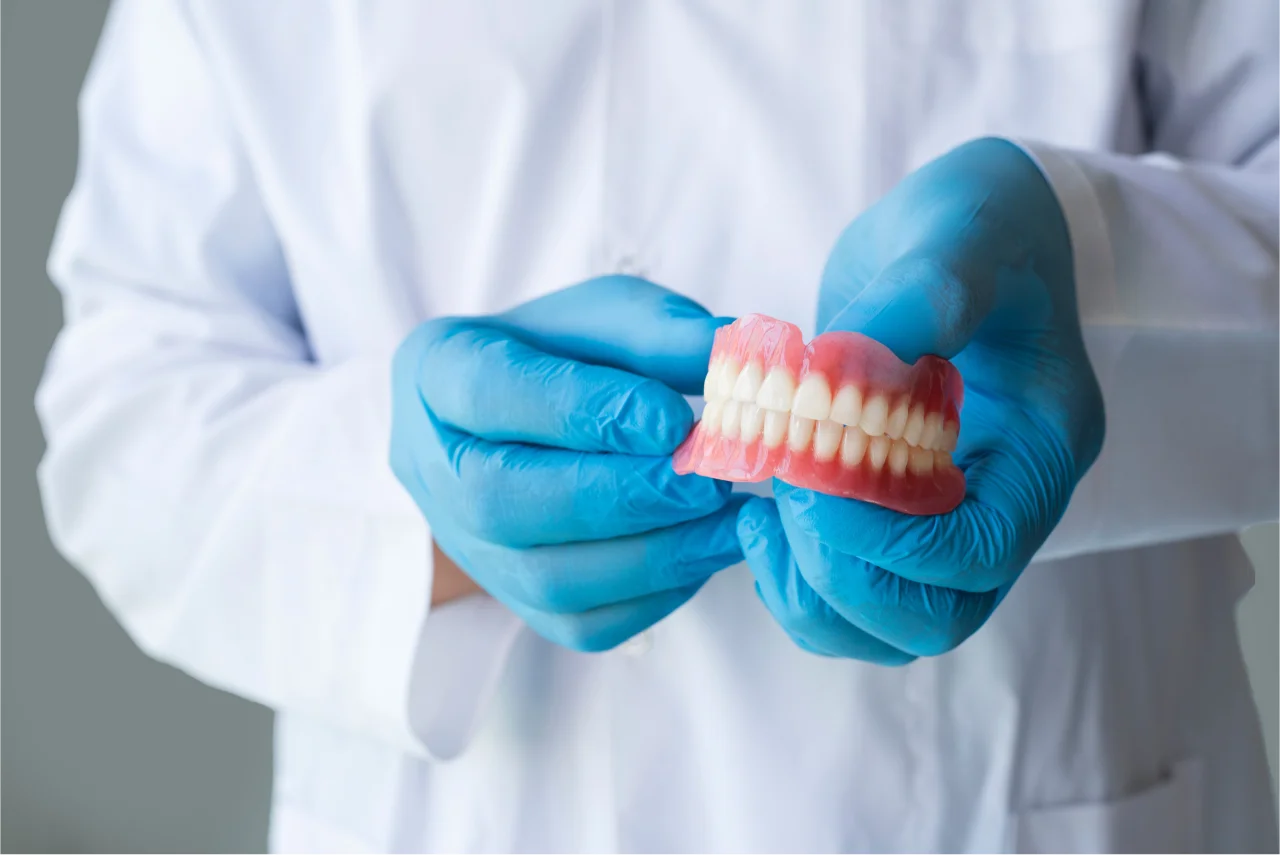 Dentist in white coat holding set of dentures in clinical setting