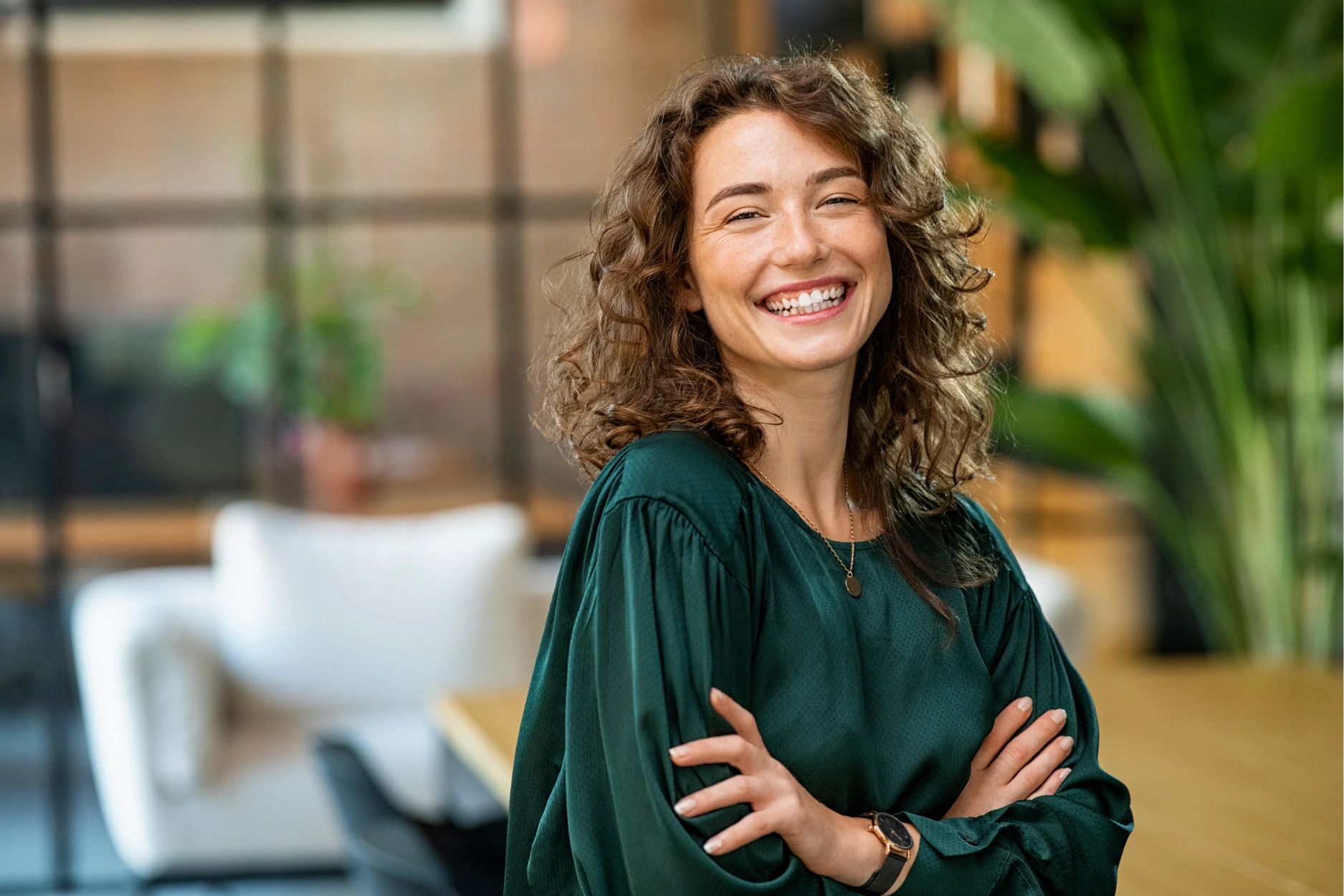 Smiling woman with curly hair standing with arms crossed in dental office