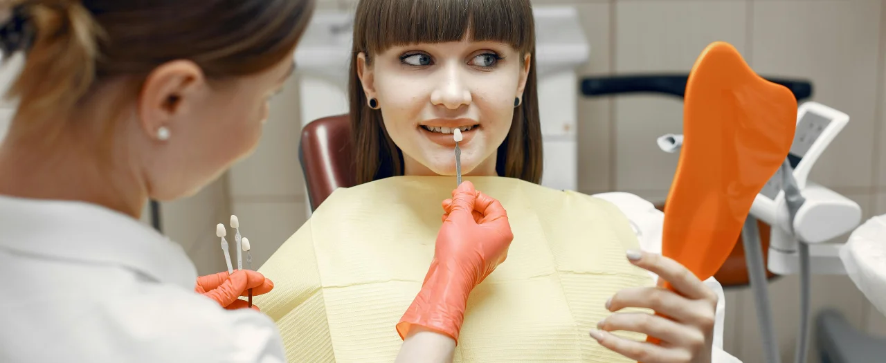 Smiling woman holding mirror looking at her teeth in dental office