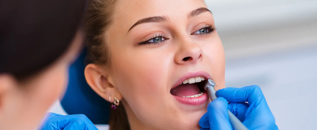 Woman receiving dental examination with dentist wearing blue gloves checking her teeth