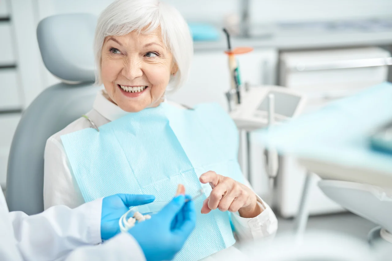 Senior woman smiling in dental chair with dentist wearing blue gloves beside her