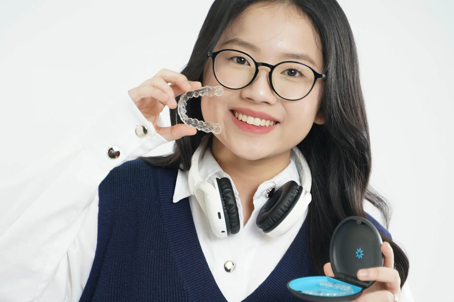 Smiling teenage girl wearing glasses and braces holding orthodontic aligner case