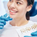 Dentist showing porcelain veneer shade options to a smiling patient during a veneers consultation at Higher Ground Dentistry in Upland CA