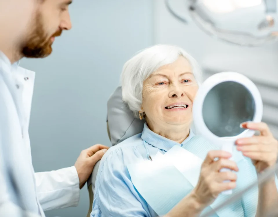 Senior woman smiling at mirror after dental implants procedure at Higher Ground Dentistry in Upland CA