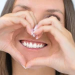 Woman making heart shape with hands showing healthy smile during National Smile Month at Higher Ground Dentistry dentist upland ca