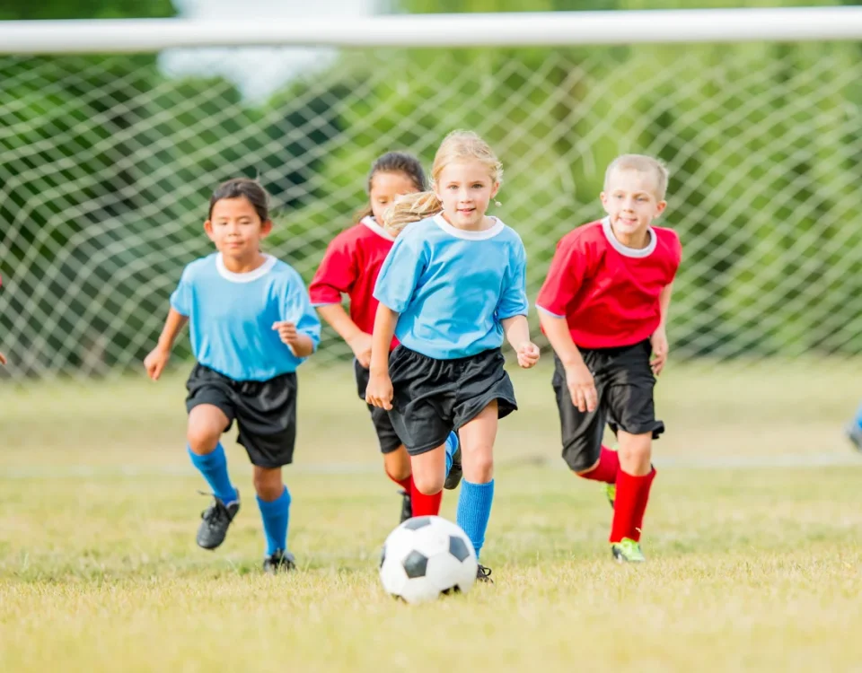 Kids playing soccer during summer sports season representing the need for dental protection and custom mouth guards to prevent cracked tooth upland injuries